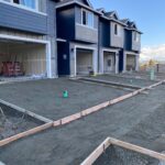 Blue and grey townhouses with concrete foundation for driveways in new construction development.