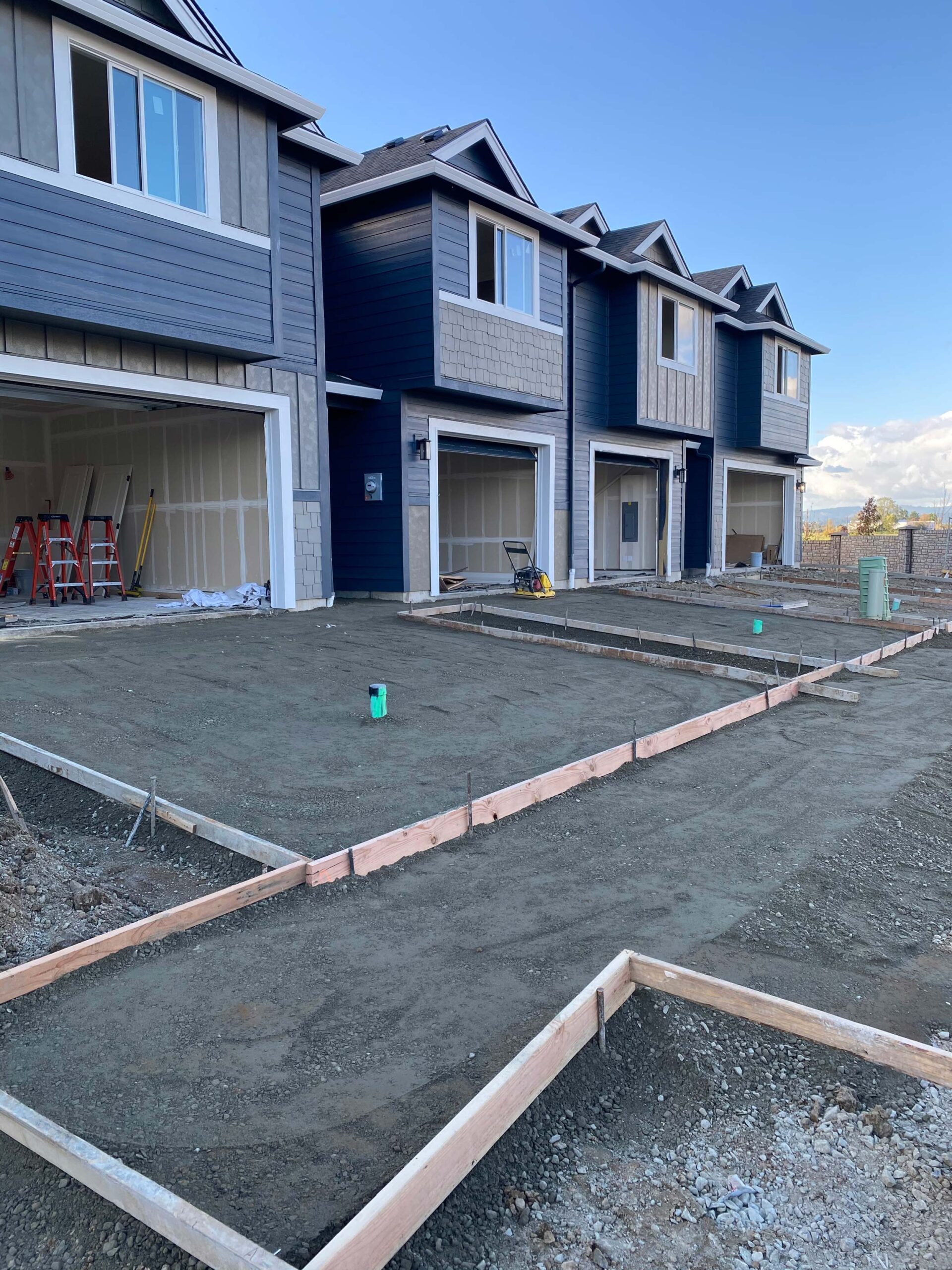 Blue and grey townhouses with concrete foundation for driveways in new construction development.