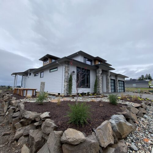 Modern grey home with gravel and boulder hardscaping on the property perimeter.